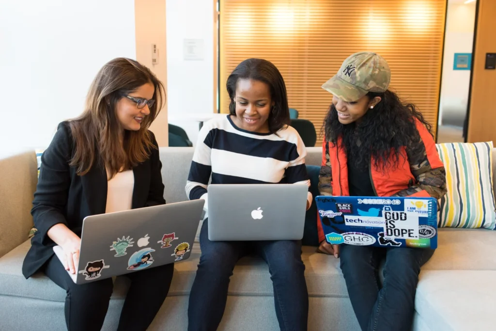 three women sitting on a sofa with laptops