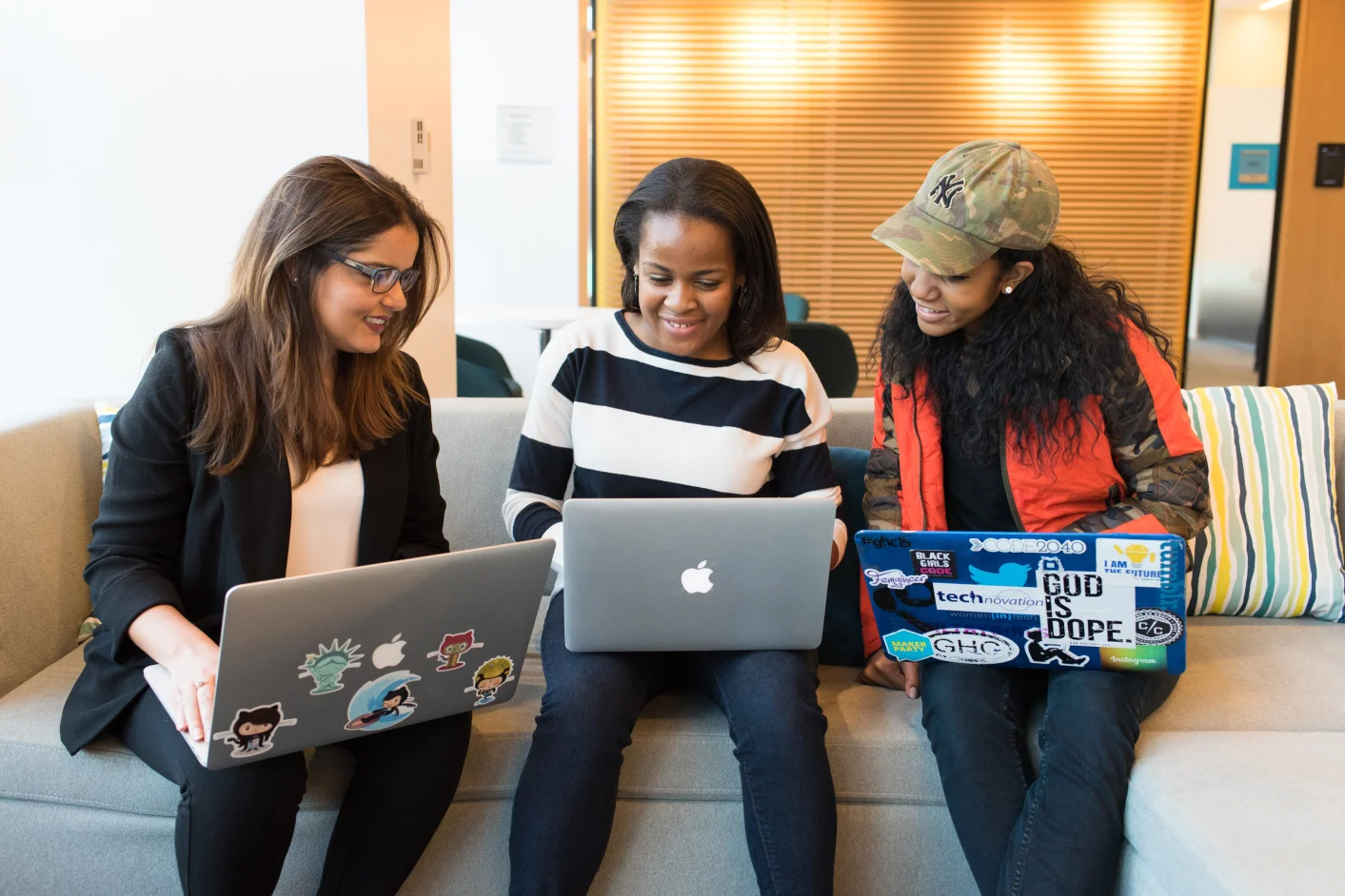 three women sitting on a sofa with laptops