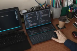 person coding on a desk with two laptops