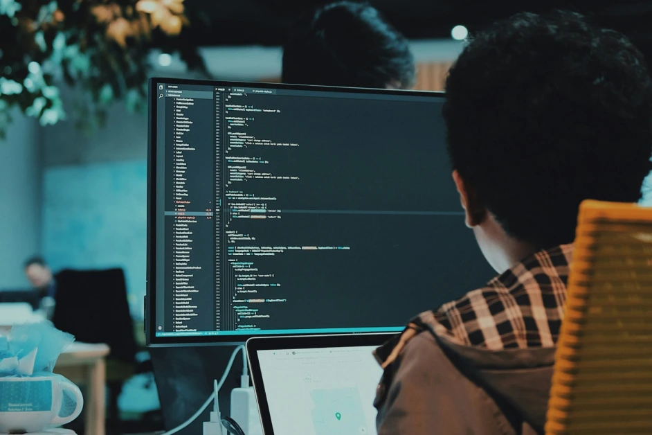 person coding on a laptop and a large monitor
