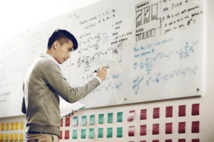 man drawing on white board working on coding problems